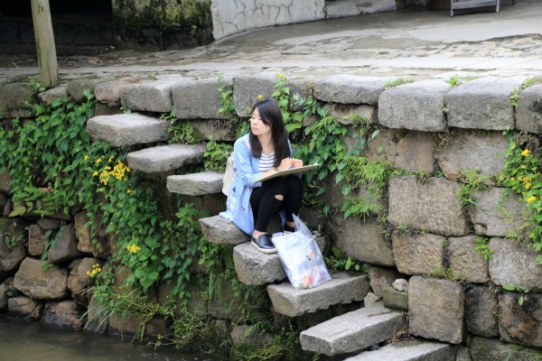 一个女孩子坐在等级上画着前面的石桥.石墩建筑设计体育图片